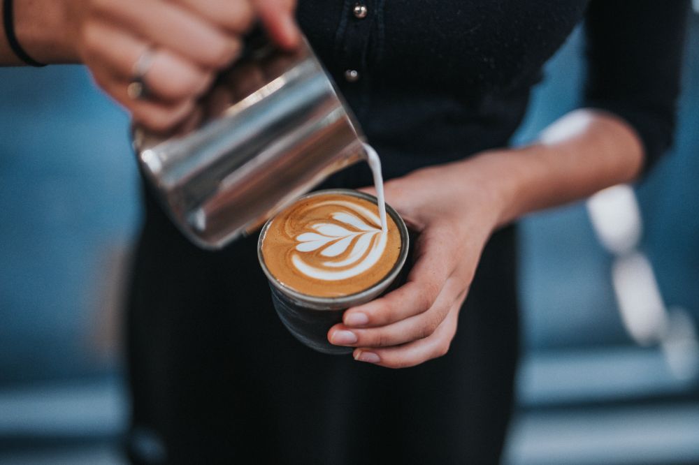 Steamed milk making a fancy design as it is poured into cup of coffee